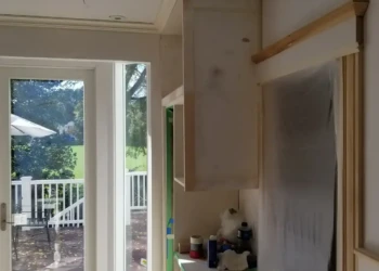 Close-up of light-colored kitchen cabinets being refinished and prepared near large glass door in Newton MA home