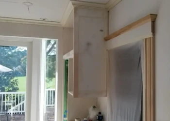 Unfinished kitchen cabinets and trim in daylight with masking and protective sheeting, during cabinet refinishing in Newton MA