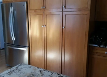 Refinished cherry wood kitchen cabinets with smooth, glossy surfaces and silver knobs next to a stainless steel refrigerator in Sudbury MA kitchen