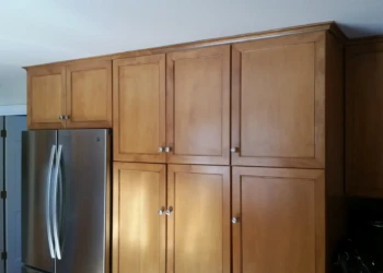 Smooth finished cherry wood kitchen cabinets with metal knobs next to stainless steel refrigerator