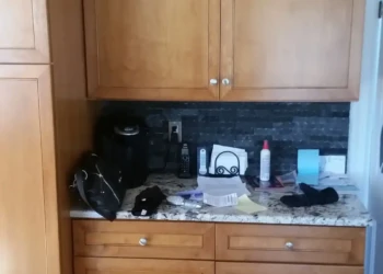 Cherry wood kitchen cabinets with flat panel doors and silver knobs above granite countertop with black stone backsplash in Sudbury MA