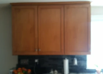 Original cherry wood kitchen cabinets above black tiled backsplash with natural light from window in Sudbury kitchen