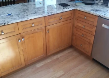 L-shaped cherry wood kitchen cabinets with a smooth, warm finish below a granite countertop near a stainless steel dishwasher.