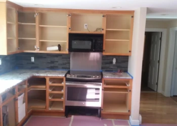 Open kitchen cabinets missing doors and drawers around stainless steel oven and microwave ready for cabinet refinishing in Sudbury MA