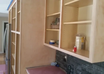 Unfinished kitchen cabinets in a Sudbury MA home, prepped for cabinet refinishing with visible sanding and taping.