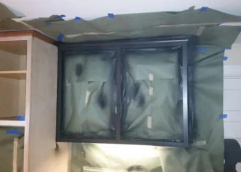 Kitchen wall cabinets masked with protective covering during cabinet refinishing in Sudbury MA