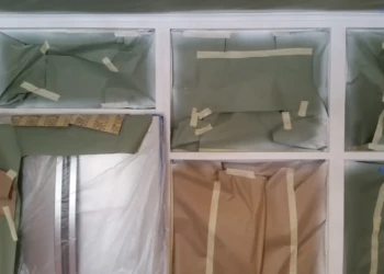 Wood kitchen cabinets with sections masked off using paper and tape during cabinet refinishing in Sudbury MA