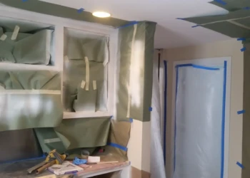 Kitchen cabinetry masked and covered with protective paper and tape during cabinet refinishing preparation in Sudbury MA