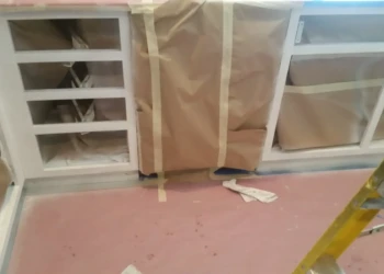 Kitchen base cabinets in Sudbury MA mid-prep for cabinet refinishing with masked sections and sanding underway