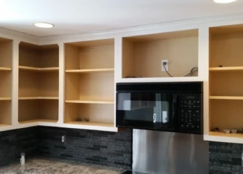 Empty upper kitchen cabinets and shelves around a black microwave above a granite countertop in Sudbury MA kitchen