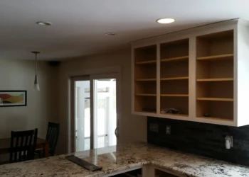 Open kitchen wall cabinets without doors installed above granite countertop near window and dining area in Sudbury MA
