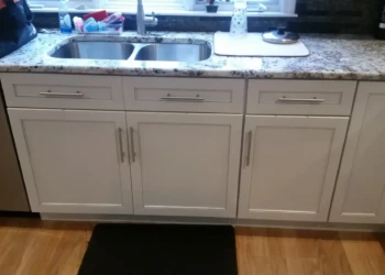 Kitchen cabinets with white painted finish and granite countertop below a window in a Sudbury MA kitchen