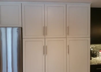 Grey kitchen cabinets with sleek metal handles next to stainless steel refrigerator, refinished with smooth durable coating in Sudbury MA