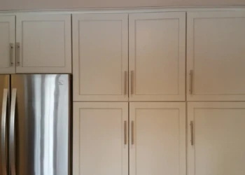 Smooth light gray kitchen cabinets with modern handles beside stainless steel refrigerator in Sudbury MA kitchen
