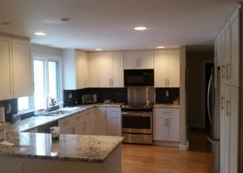 White kitchen cabinets with modern hardware in a softly lit kitchen featuring granite countertops and stainless steel appliances