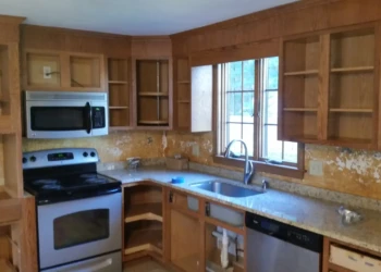 Unpainted wooden kitchen cabinets around stove and sink area in Westford kitchen before cabinet refinishing painting
