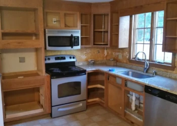 Empty unpainted wooden kitchen cabinets and drawers surrounding a stainless steel stove, microwave, and dishwasher in Westford kitchen