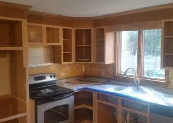 Unpainted wooden kitchen cabinets installed around stove and window in Westford kitchen during cabinet refinishing painting project