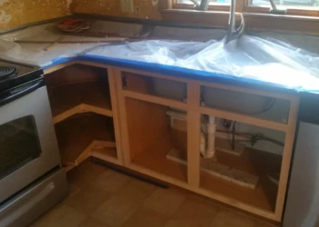 Kitchen base cabinets without doors under countertop covered with plastic in Westford MA kitchen during cabinet refinishing painting