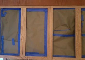 Oak kitchen cabinet frames with glass openings masked with brown paper and blue painter's tape for cabinet refinishing painting in Westford MA
