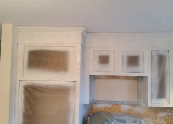 Kitchen cabinets covered partially with protective plastic sheeting during cabinet refinishing painting in Westford