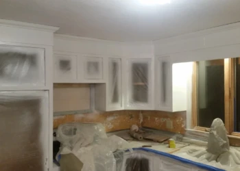 White kitchen cabinets in mid-stage of cabinet refinishing painting with protective plastic coverings in Westford MA