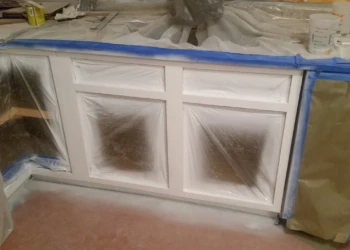 Partially painted kitchen cabinets with plastic masking protecting surrounding areas during cabinet refinishing painting in Westford MA