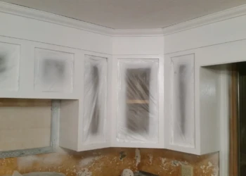 White kitchen cabinets with cabinet doors and glass panels covered in plastic masking in Westford Massachusetts