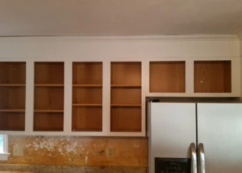 Kitchen upper cabinet frames painted white with bare wood interiors above countertop and stainless steel refrigerator in Westford MA