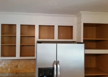 Kitchen cabinets with white painted trim and natural wood interior shelves above a stainless steel refrigerator in Westford MA
