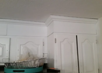Corner view of white painted kitchen cabinets with ornate trim and crown molding in Westford MA