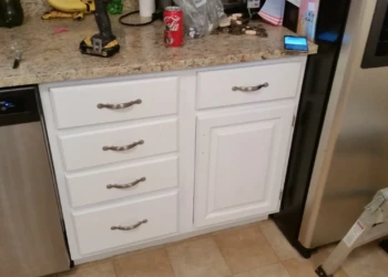 White painted kitchen cabinet drawers and door with silver handles between stainless steel dishwasher and refrigerator