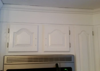 Section of white-painted kitchen cabinets above a stainless steel stove vent in a Westford home