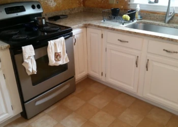 Freshly refinished white kitchen cabinets with silver handles next to stainless steel stove and sink in Westford, MA home