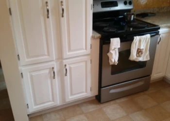 White refinished kitchen cabinets surrounding a stainless steel stove with towels in Westford kitchen