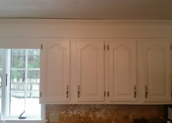 White painted kitchen cabinets with ornate paneling above a countertop near a window in a Westford kitchen