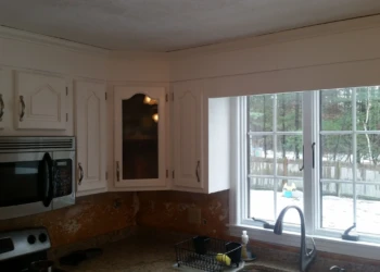 White painted kitchen cabinets above countertop with stainless steel microwave and window in Westford kitchen