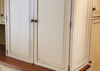 Cream-colored kitchen cabinets with crown molding and detailed trim, featuring a wood countertop and multiple cabinet doors