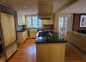 Kitchen featuring refinished cabinets in creamy Benjamin Moore Capitol White with gold hardware, a black countertop island, and hardwood floors in Weston MA