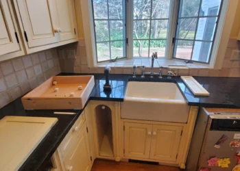Close-up of farmhouse kitchen sink surrounded by refinished Benjamin Moore Capitol White cabinets and black granite countertop in Weston MA kitchen