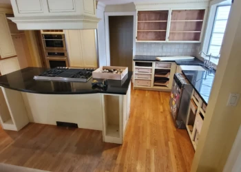 Kitchen with cream-colored cabinets refinished in Benjamin Moore Capitol White, black countertops, hardwood floor in Weston MA