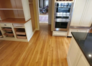 Close-up of refurbished kitchen cabinets with white Benjamin Moore finish and gold hardware next to kitchen island with black countertop