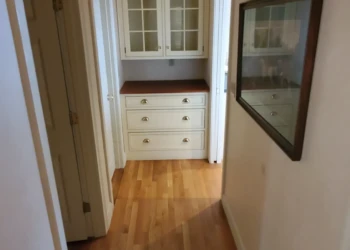 Hallway with custom built-in cabinet featuring glass doors and gold knobs, refinished in Capitol White in Weston MA