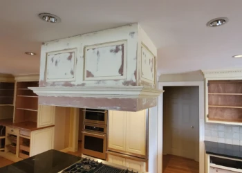 Kitchen cabinets and range hood in Weston home during cabinet refinishing process with unfinished surfaces and woodwork exposed