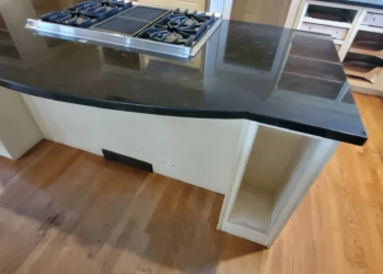Kitchen island with black countertop and gas stove, light-colored refinished cabinets, and hardwood floor in Weston MA kitchen