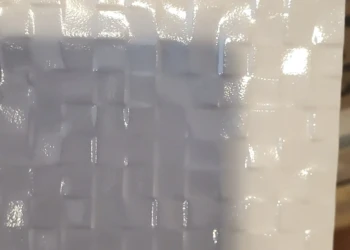 Porcelanosa glossy white textured tile sample held by hand, suitable for kitchen or bath upgrades.