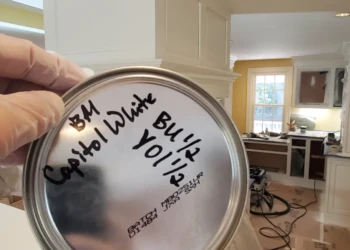Hand holding paint can lid labeled Benjamin Moore Capitol White in a kitchen under cabinet refinishing project in Weston MA