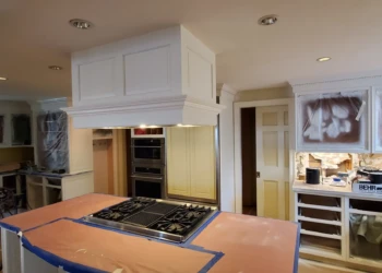 Kitchen space with cabinets covered for refinishing and protective paper on island countertop during remodeling in Weston MA