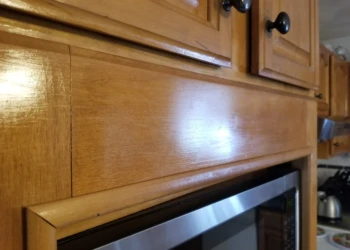 Close-up of wooden kitchen cabinet door with smooth natural wood finish above a built-in microwave