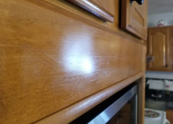Close-up of a worn wooden kitchen cabinet surface with visible scratches and uneven finish
